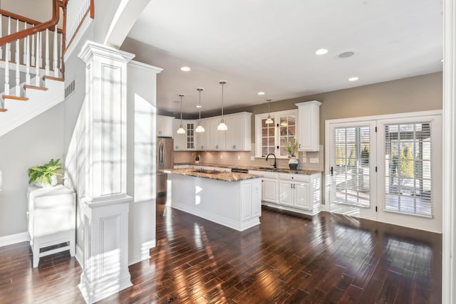 kitchen featuring tasteful backsplash, hanging light fixtures, light stone countertops, white cabinets, and a center island