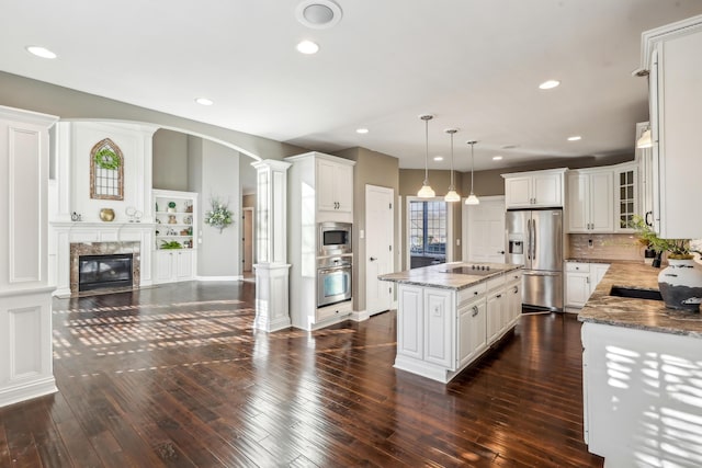 kitchen featuring decorative columns, appliances with stainless steel finishes, decorative light fixtures, light stone counters, and a center island