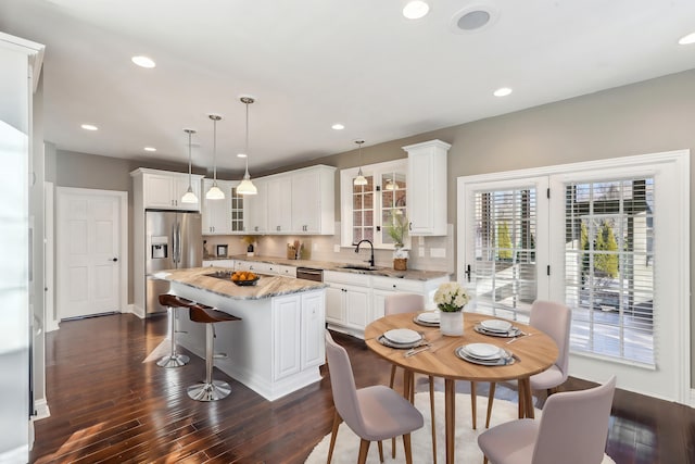 kitchen featuring light stone countertops, white cabinets, a kitchen island, decorative light fixtures, and sink