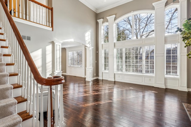 foyer entrance with a high ceiling, crown molding, dark hardwood / wood-style floors, and ornate columns