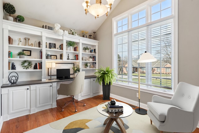 office space featuring built in desk, light wood-type flooring, a notable chandelier, and vaulted ceiling