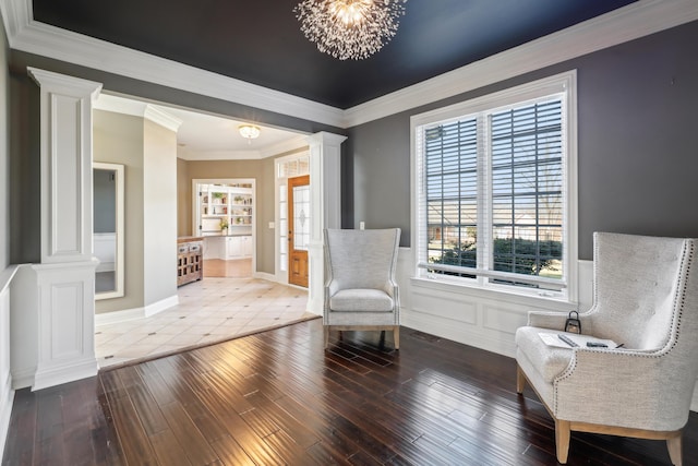 unfurnished room featuring crown molding, hardwood / wood-style floors, an inviting chandelier, and ornate columns