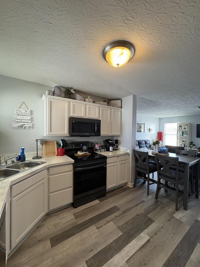 kitchen featuring sink, wood-type flooring, a textured ceiling, white cabinets, and black appliances