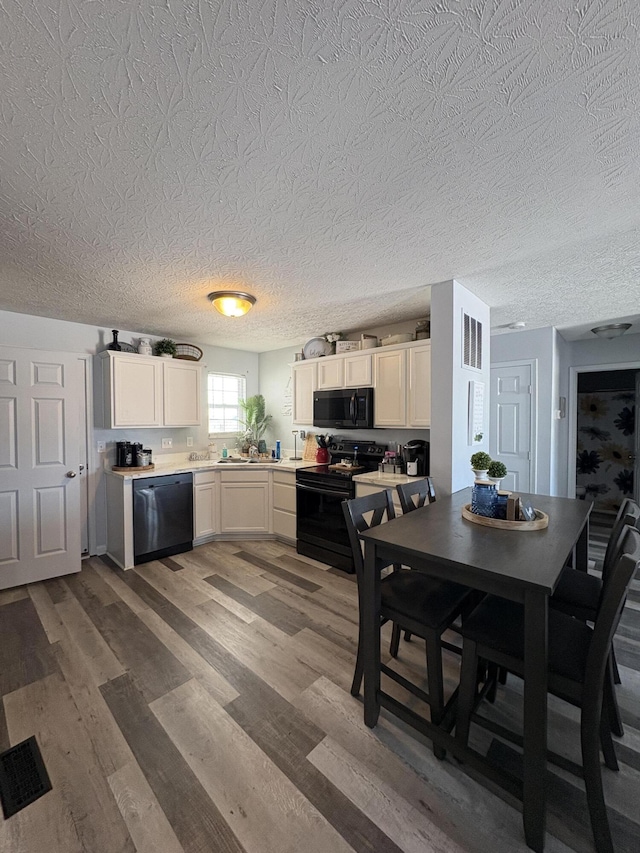 kitchen featuring hardwood / wood-style floors, white cabinets, black appliances, and a textured ceiling