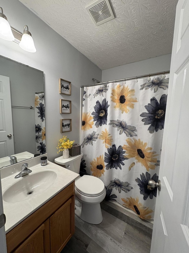 bathroom featuring walk in shower, hardwood / wood-style floors, a textured ceiling, toilet, and vanity