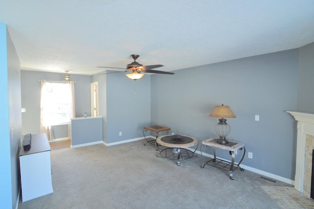 sitting room featuring a tiled fireplace, ceiling fan, and light colored carpet