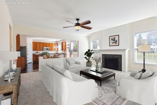 living room with a fireplace, ceiling fan, a wealth of natural light, and light colored carpet