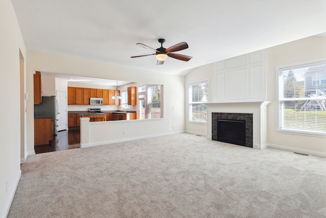 unfurnished living room with a tile fireplace, light colored carpet, ceiling fan, and a wealth of natural light