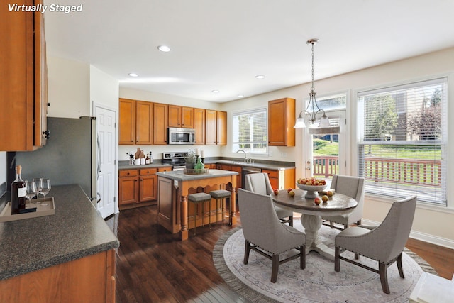 kitchen featuring stainless steel appliances, dark hardwood / wood-style flooring, a wealth of natural light, a kitchen island, and decorative light fixtures