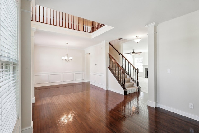 empty room with ornamental molding, dark hardwood / wood-style flooring, ceiling fan with notable chandelier, and ornate columns