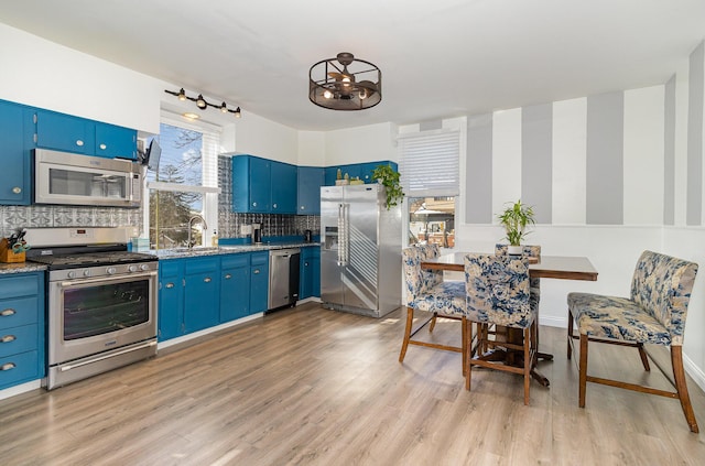 kitchen featuring light hardwood / wood-style floors, decorative backsplash, blue cabinets, appliances with stainless steel finishes, and sink