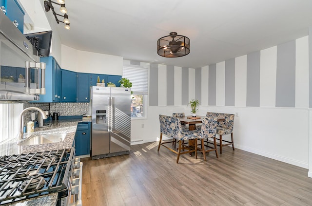 kitchen with hardwood / wood-style floors, appliances with stainless steel finishes, sink, blue cabinets, and tasteful backsplash