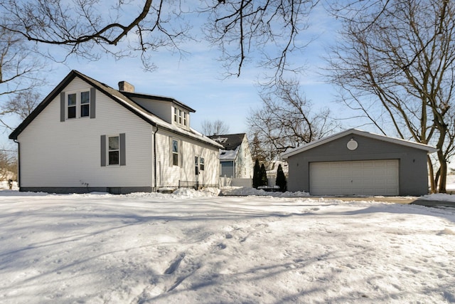 snow covered property featuring a garage and an outbuilding