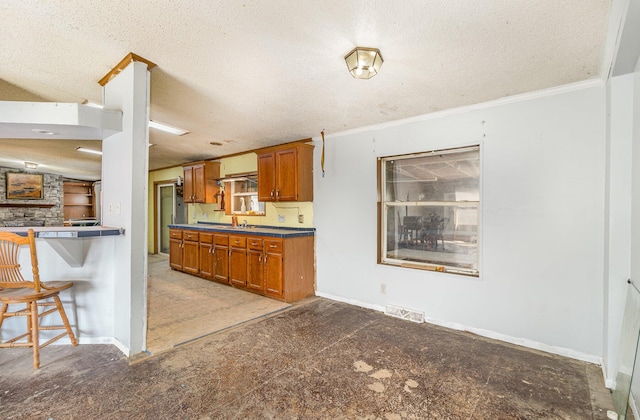 kitchen featuring visible vents, a textured ceiling, brown cabinetry, and crown molding