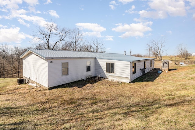 back of house featuring a lawn, cooling unit, and metal roof