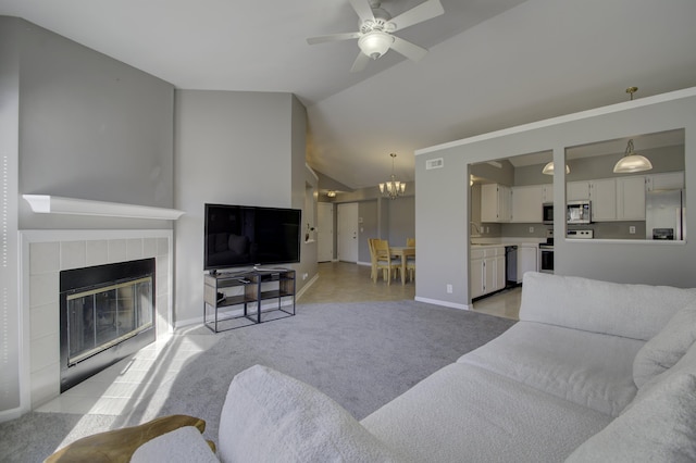 carpeted living room with ceiling fan with notable chandelier, a tiled fireplace, sink, and vaulted ceiling