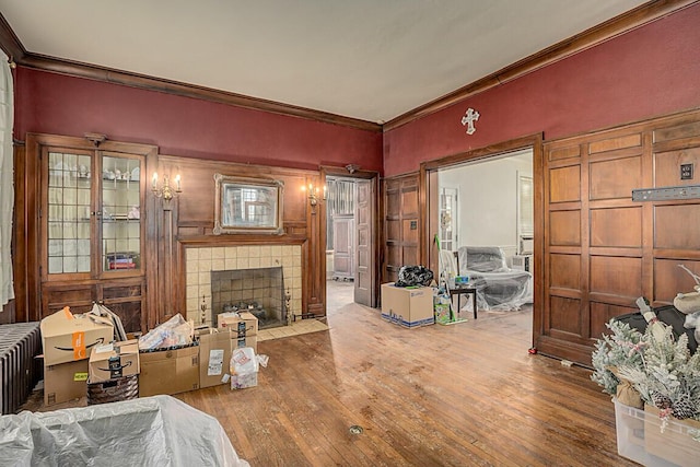 living room with radiator, a tiled fireplace, ornamental molding, and light hardwood / wood-style floors