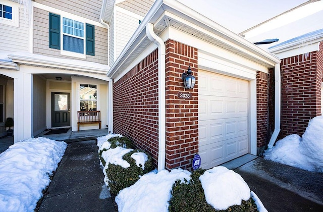 snow covered property entrance with covered porch and a garage