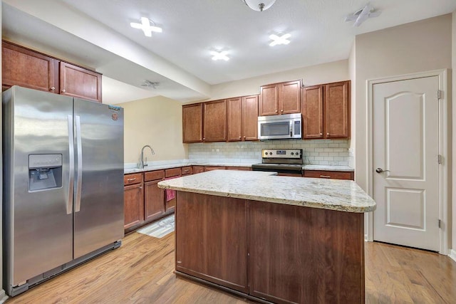 kitchen with light hardwood / wood-style floors, a kitchen island, decorative backsplash, light stone countertops, and appliances with stainless steel finishes