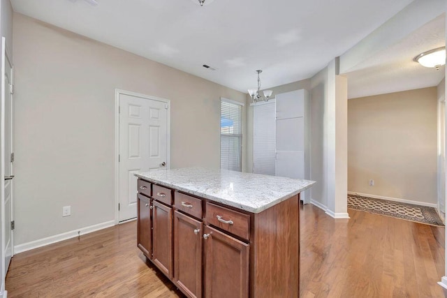 kitchen with a kitchen island, light hardwood / wood-style flooring, light stone counters, and hanging light fixtures