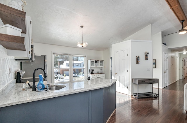 kitchen with hanging light fixtures, kitchen peninsula, light stone countertops, sink, and backsplash