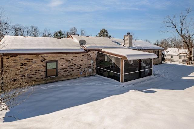 snow covered back of property featuring a sunroom