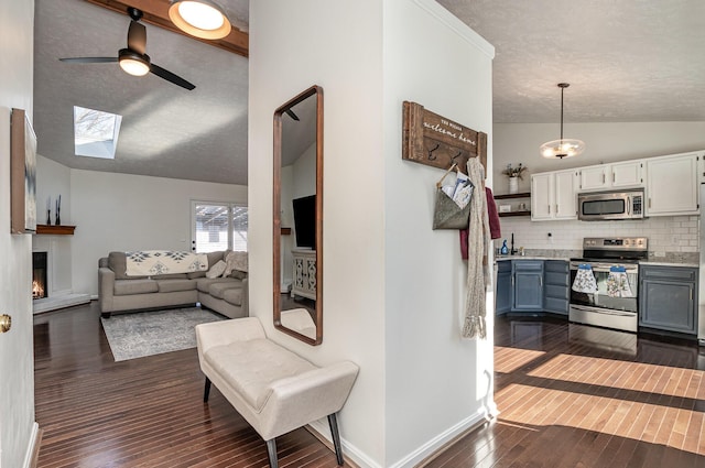 interior space with pendant lighting, dark hardwood / wood-style floors, stainless steel appliances, lofted ceiling with skylight, and backsplash