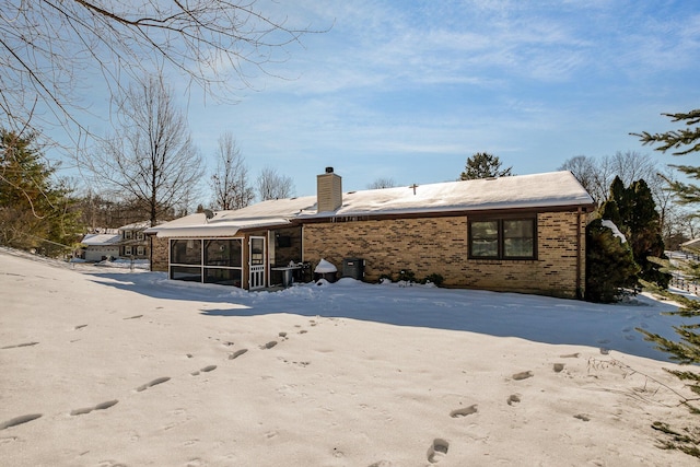 snow covered back of property with a sunroom and central AC unit