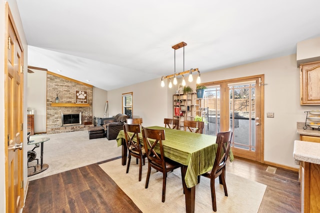 dining area with vaulted ceiling, a brick fireplace, and light hardwood / wood-style floors