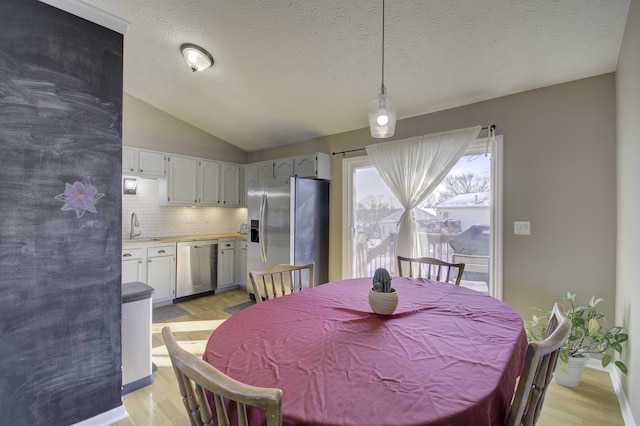 dining space with a textured ceiling, lofted ceiling, light hardwood / wood-style flooring, and sink