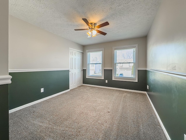 carpeted spare room featuring baseboards, a textured ceiling, and a ceiling fan