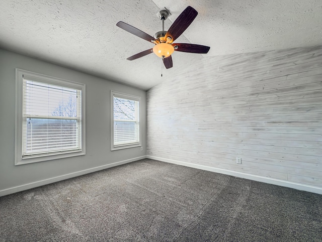 carpeted empty room with ceiling fan, vaulted ceiling, baseboards, and a textured ceiling