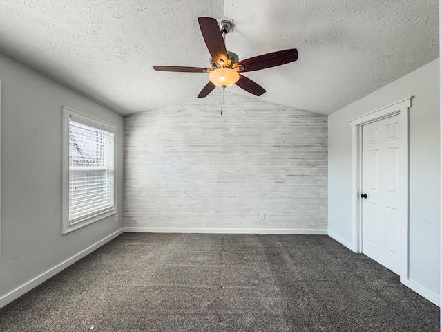 carpeted spare room with wooden walls, a textured ceiling, lofted ceiling, and ceiling fan