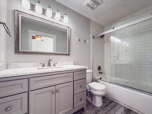 full bathroom featuring toilet, a textured ceiling, wood finished floors, enclosed tub / shower combo, and vanity