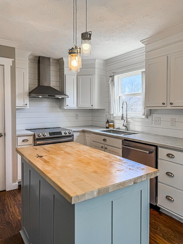 kitchen with a center island, wall chimney range hood, appliances with stainless steel finishes, wood counters, and a sink