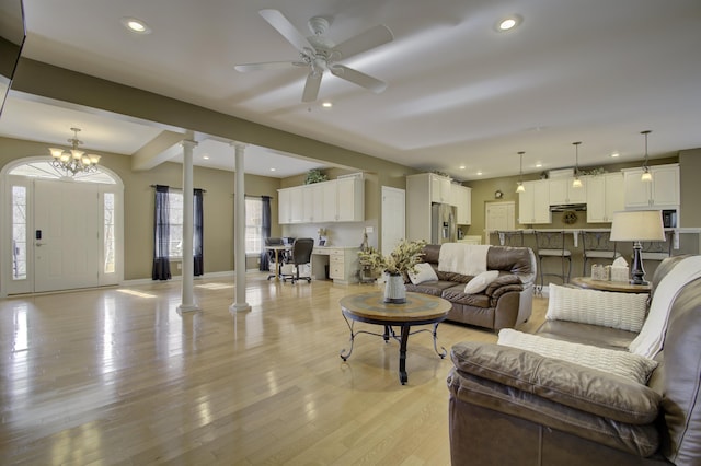 living room with ceiling fan with notable chandelier, light wood-type flooring, and a healthy amount of sunlight