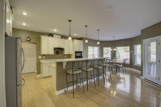 kitchen with stainless steel refrigerator, light wood-type flooring, a kitchen island, white cabinetry, and decorative light fixtures