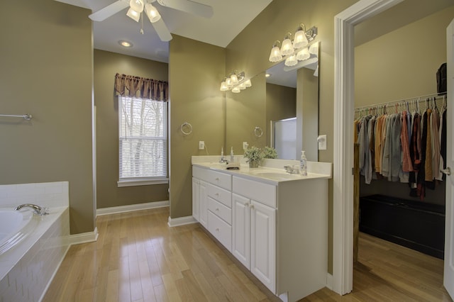 bathroom featuring hardwood / wood-style flooring, ceiling fan, tiled tub, and vanity