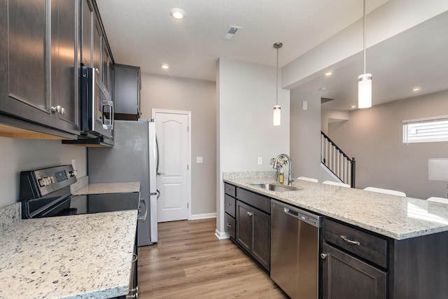 kitchen featuring light stone countertops, hanging light fixtures, dark brown cabinetry, appliances with stainless steel finishes, and sink