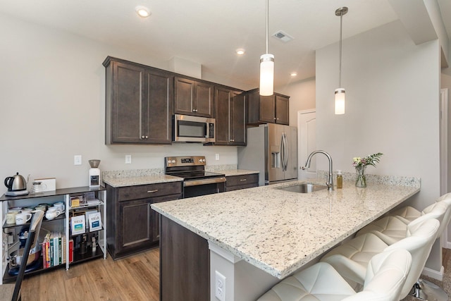 kitchen featuring stainless steel appliances, sink, decorative light fixtures, light stone counters, and a kitchen bar