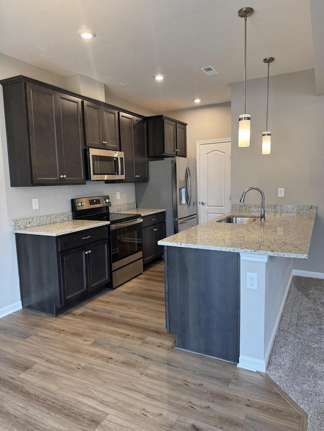 kitchen with sink, decorative light fixtures, light stone counters, light hardwood / wood-style flooring, and appliances with stainless steel finishes