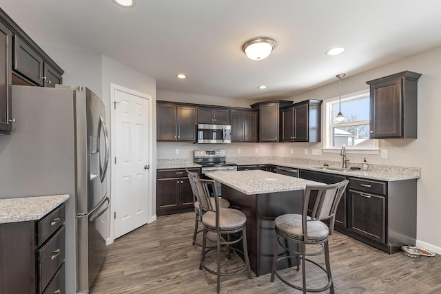 kitchen featuring hardwood / wood-style floors, appliances with stainless steel finishes, decorative light fixtures, a kitchen island, and sink