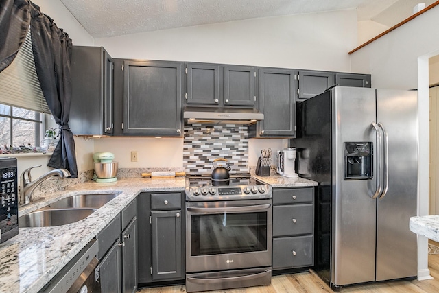 kitchen with vaulted ceiling, appliances with stainless steel finishes, tasteful backsplash, sink, and light hardwood / wood-style flooring