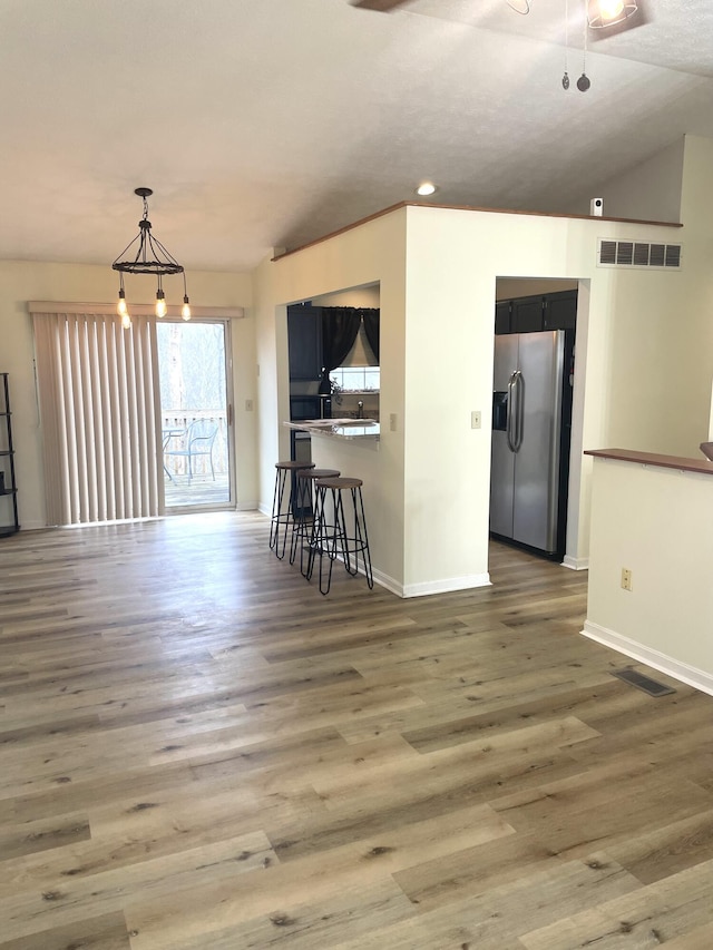 interior space featuring a breakfast bar area, decorative light fixtures, dark hardwood / wood-style floors, stainless steel fridge, and kitchen peninsula