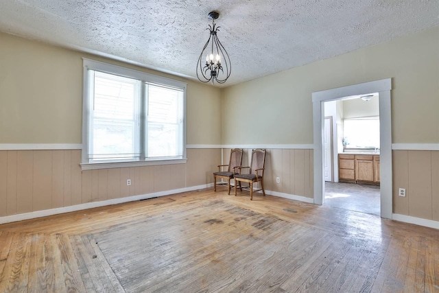 empty room with a textured ceiling, a chandelier, and light hardwood / wood-style flooring