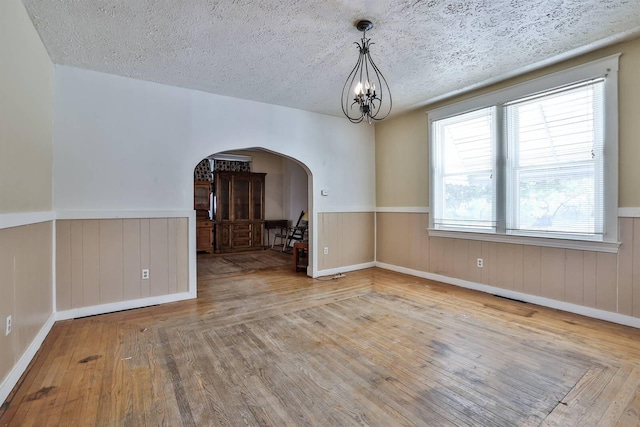 unfurnished dining area featuring light wood-type flooring, a chandelier, a textured ceiling, and wooden walls