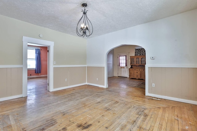 spare room with a textured ceiling, a notable chandelier, a baseboard radiator, and light hardwood / wood-style floors