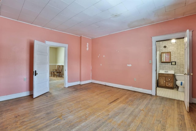 unfurnished bedroom with ensuite bath and wood-type flooring