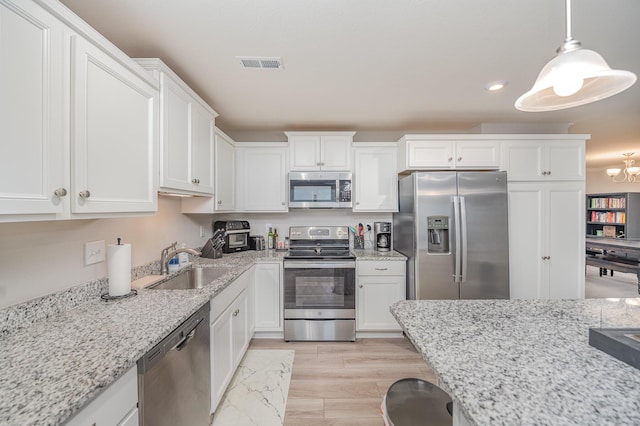 kitchen featuring pendant lighting, sink, appliances with stainless steel finishes, white cabinetry, and light stone counters