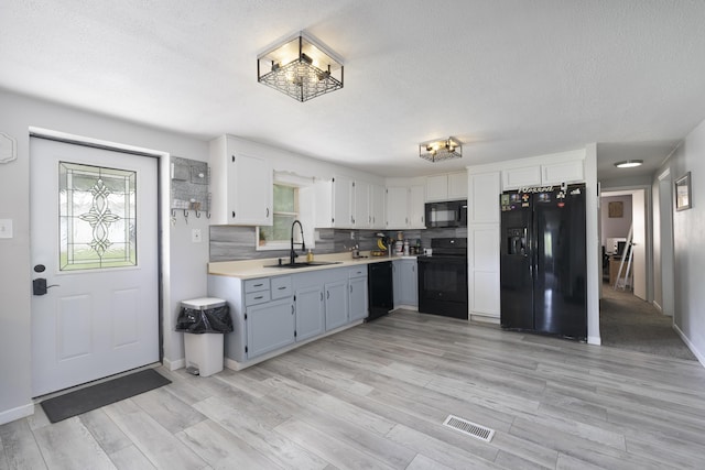 kitchen with black appliances, white cabinetry, tasteful backsplash, sink, and light wood-type flooring